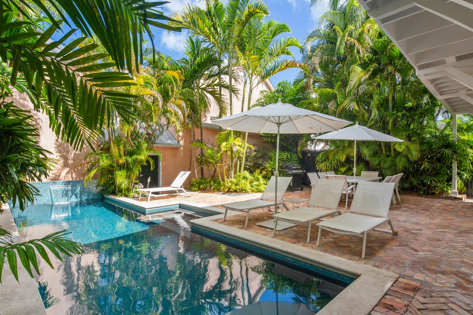 Private courtyard pool with loungers and umbrellas surrounded by lush tropical palms