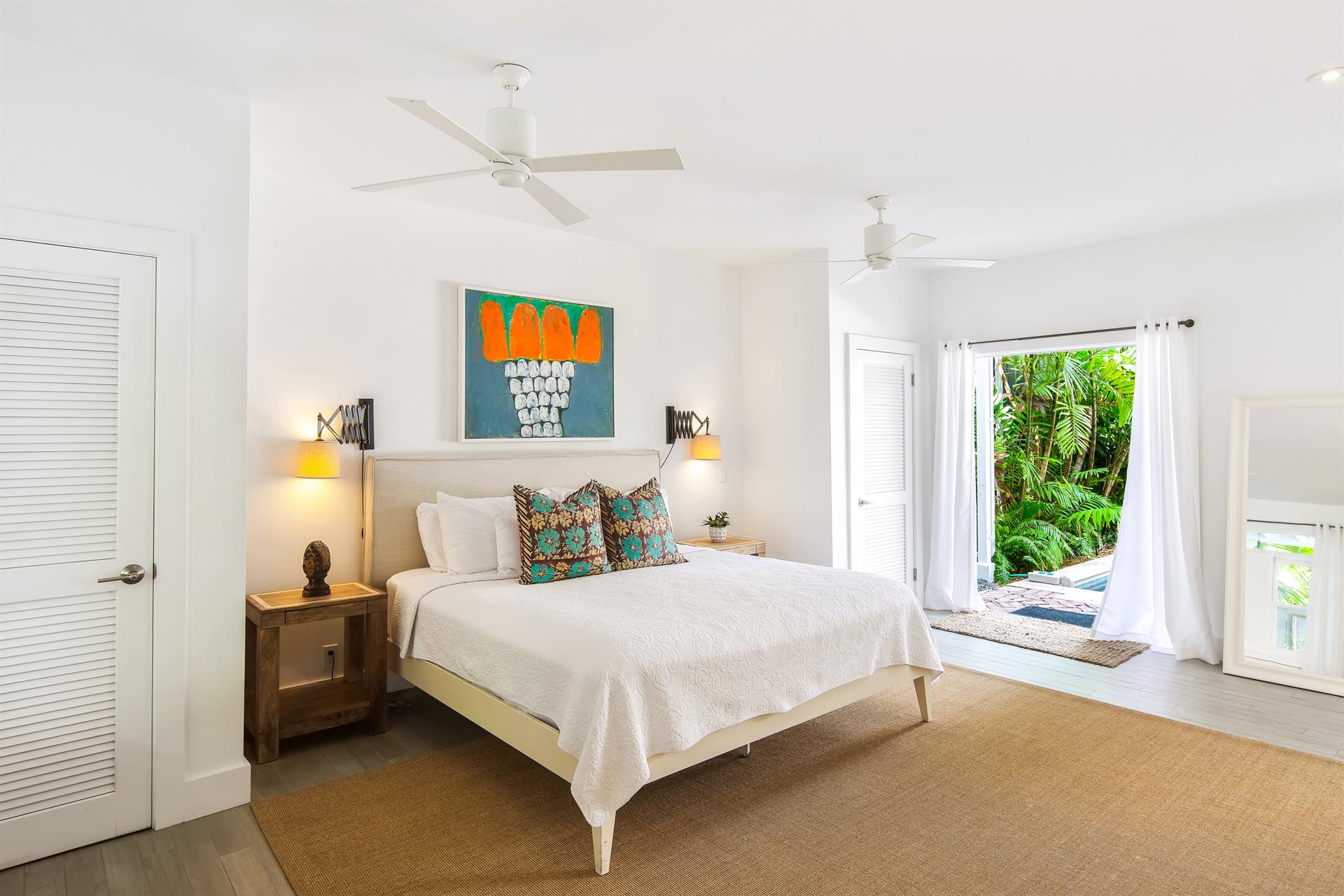 Master suite with king bed, colorful art above headboard, French doors open to a tropical garden