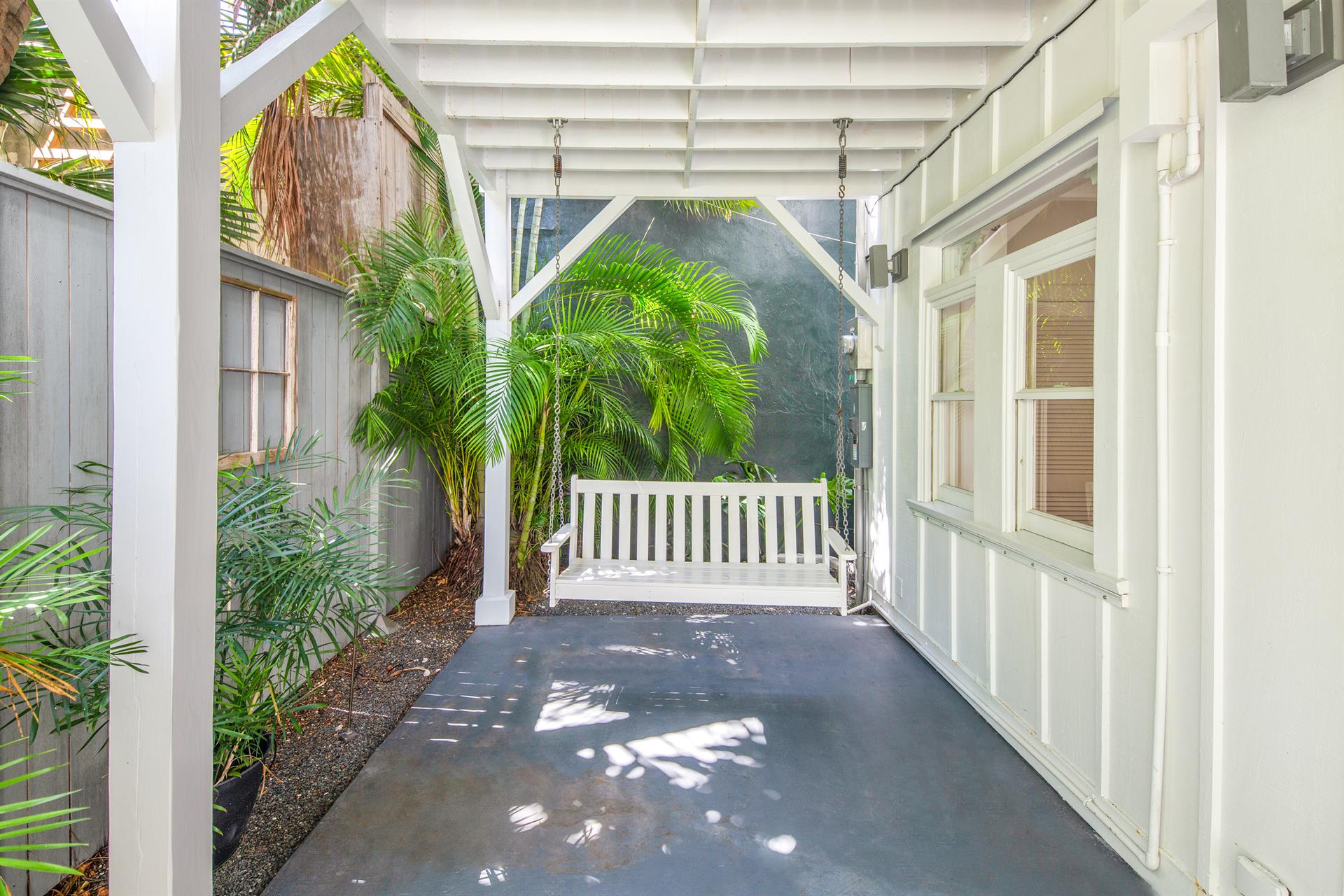 Covered side porch with a white wooden swing bench flanked by tropical palms