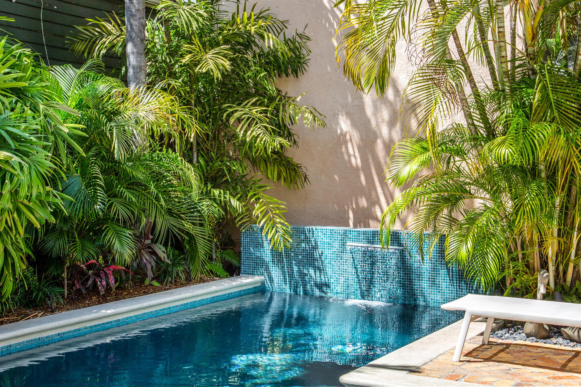 Pool water feature and mosaic tile wall nestled among dense tropical plantings
